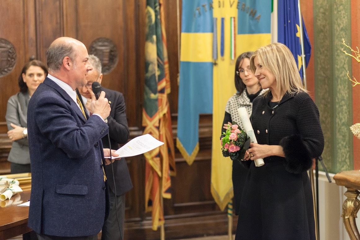Un uomo parla al microfono mentre una donna tiene in mano un mazzo di fiori.