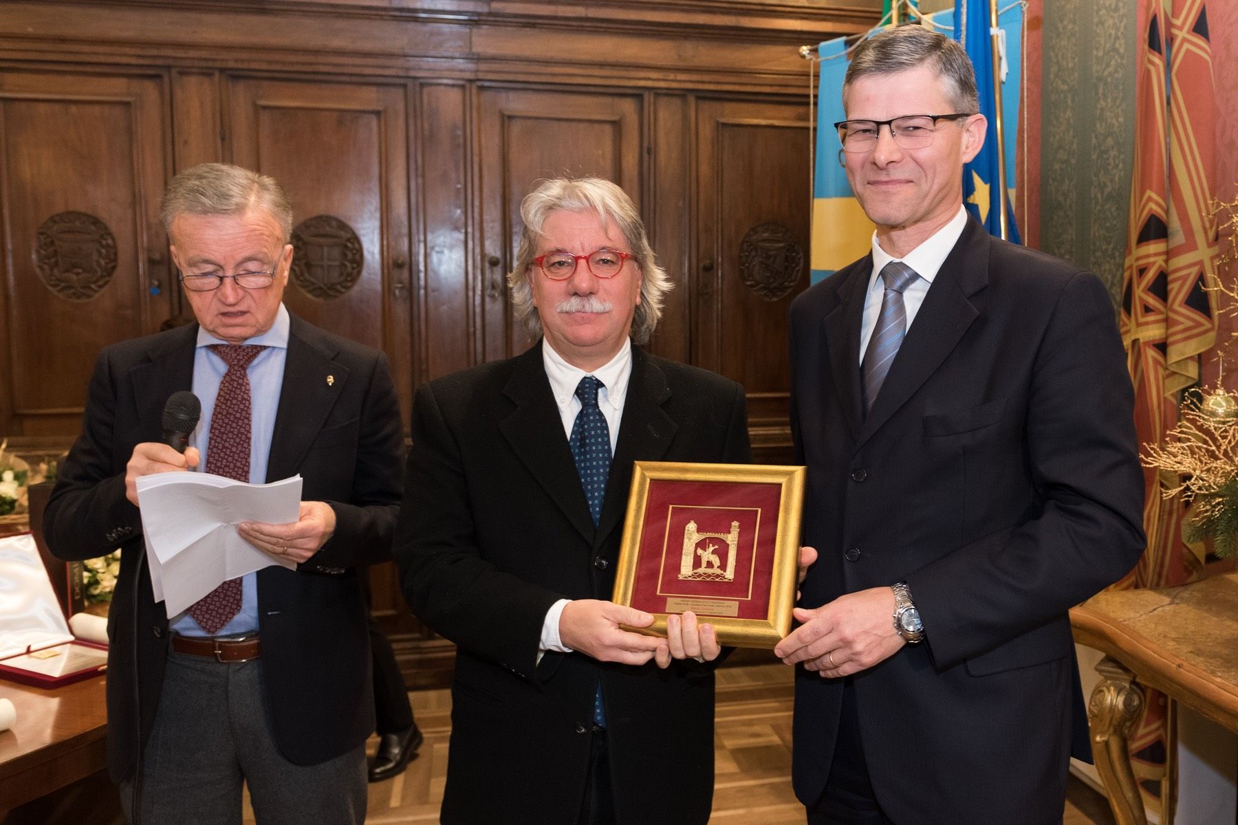 Tre uomini in giacca e cravatta sono in piedi uno accanto all'altro con in mano una foto incorniciata.