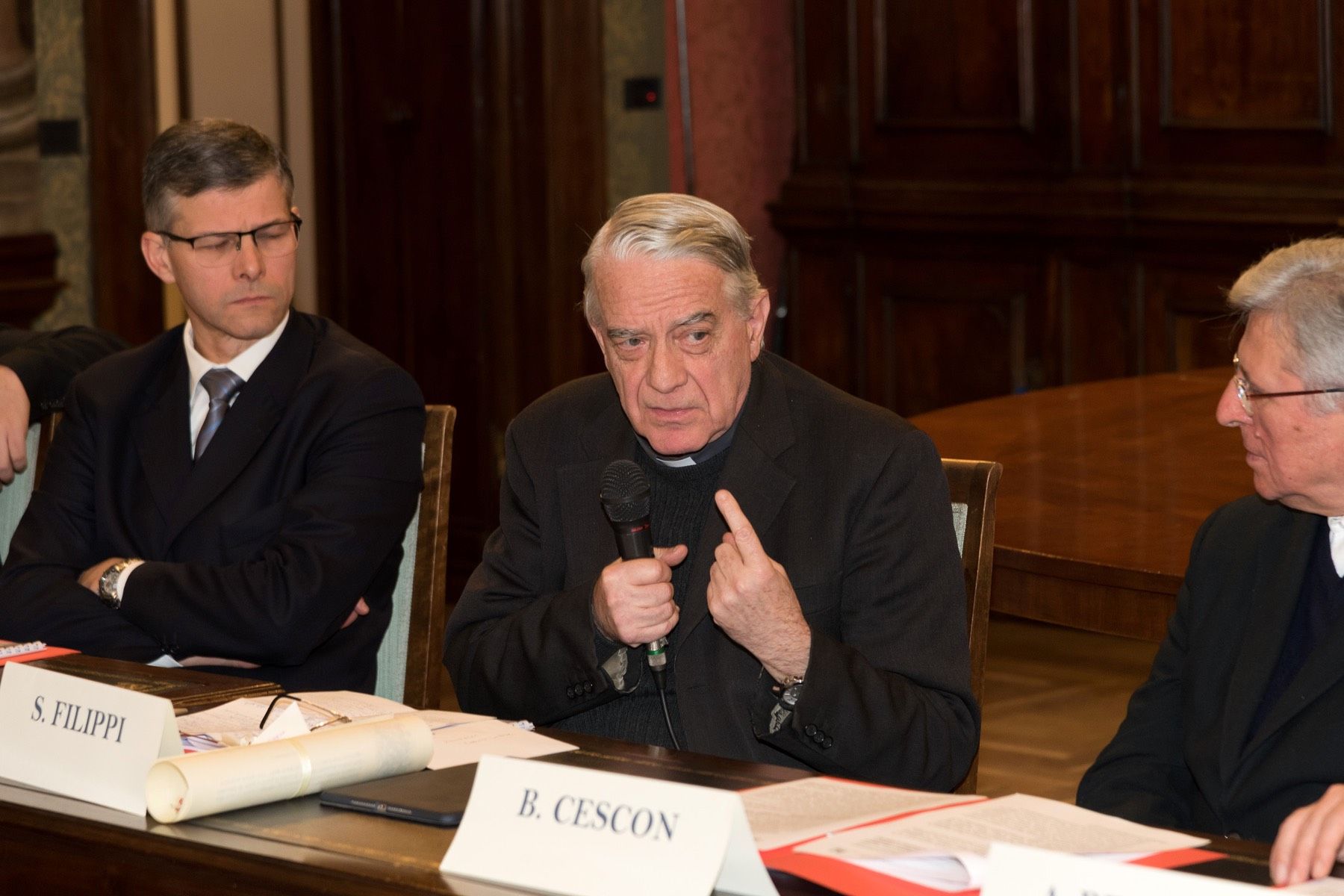 Un gruppo di uomini è seduto a un tavolo con una targhetta con il nome che dice b. cescon.