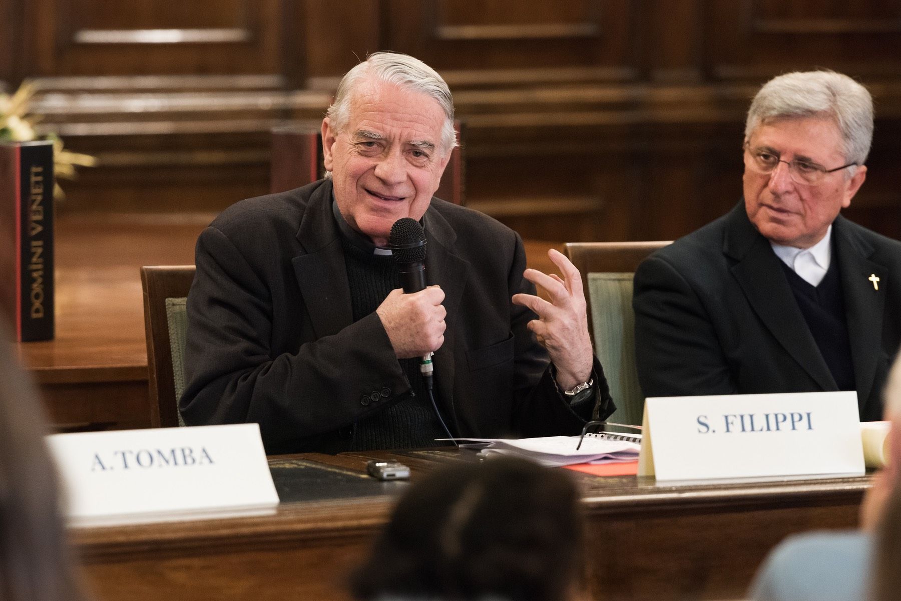 Due uomini sono seduti a un tavolo e parlano ai microfoni.