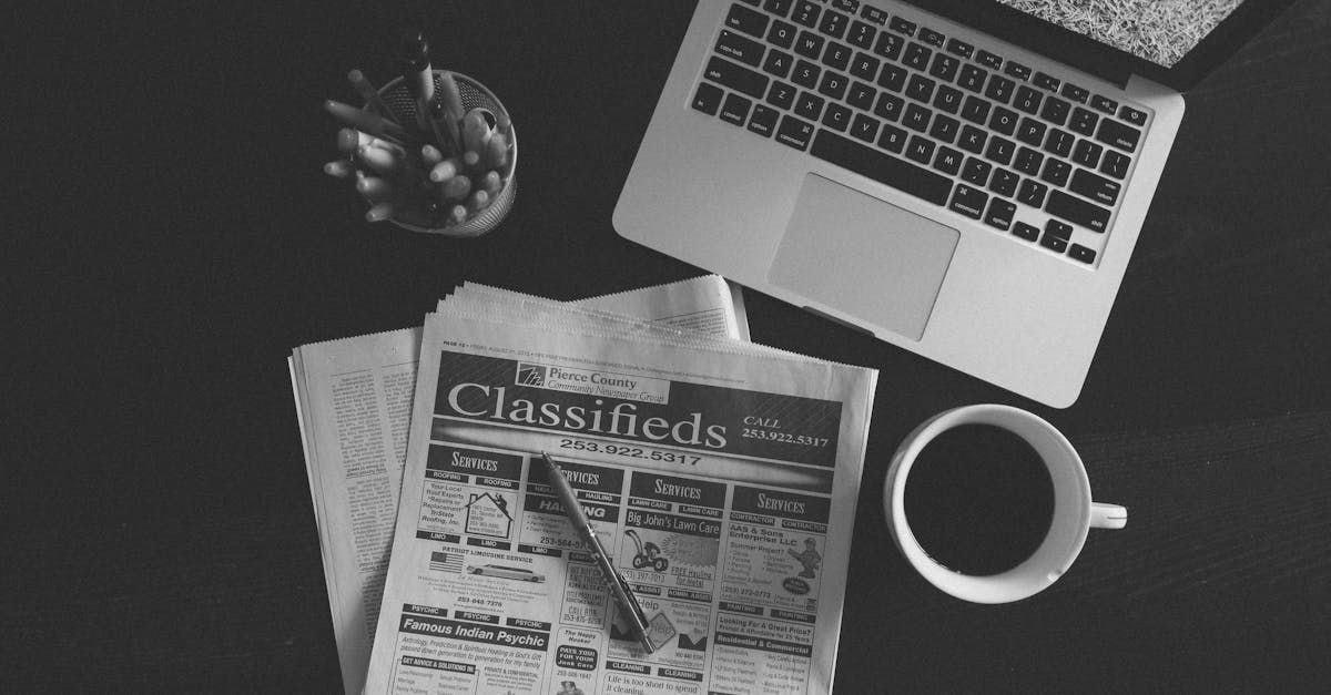 Una foto in bianco e nero di un computer portatile, un giornale, una tazza di caffè e una penna.