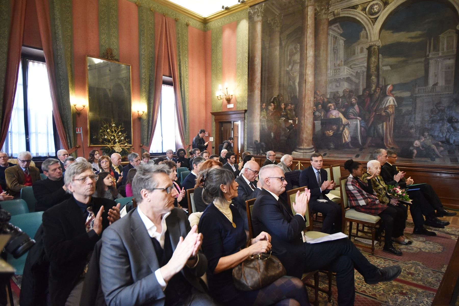 Un gruppo di persone è seduto in una stanza con un grande dipinto sul muro.