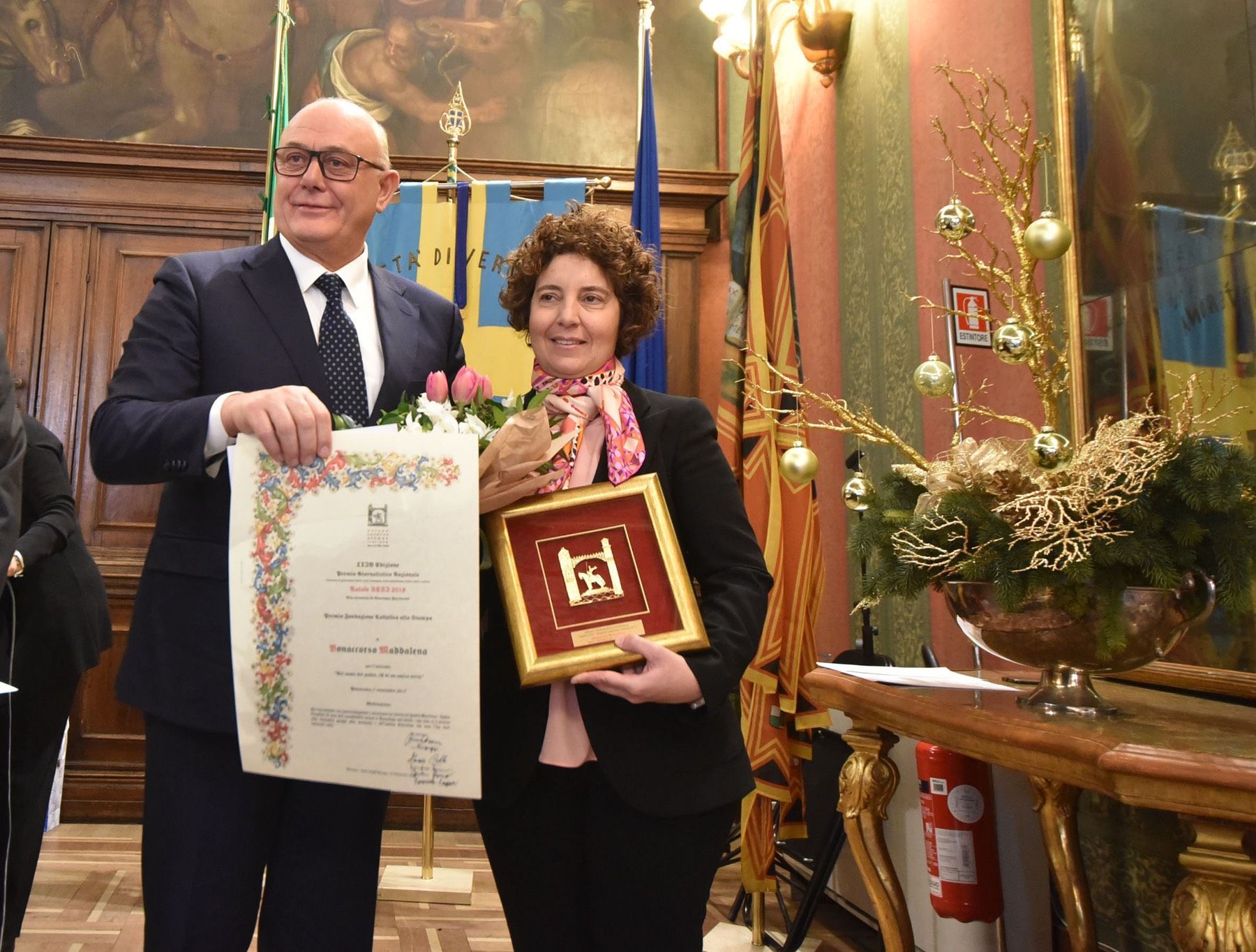 Un uomo e una donna tengono in mano un certificato e un'immagine incorniciata.
