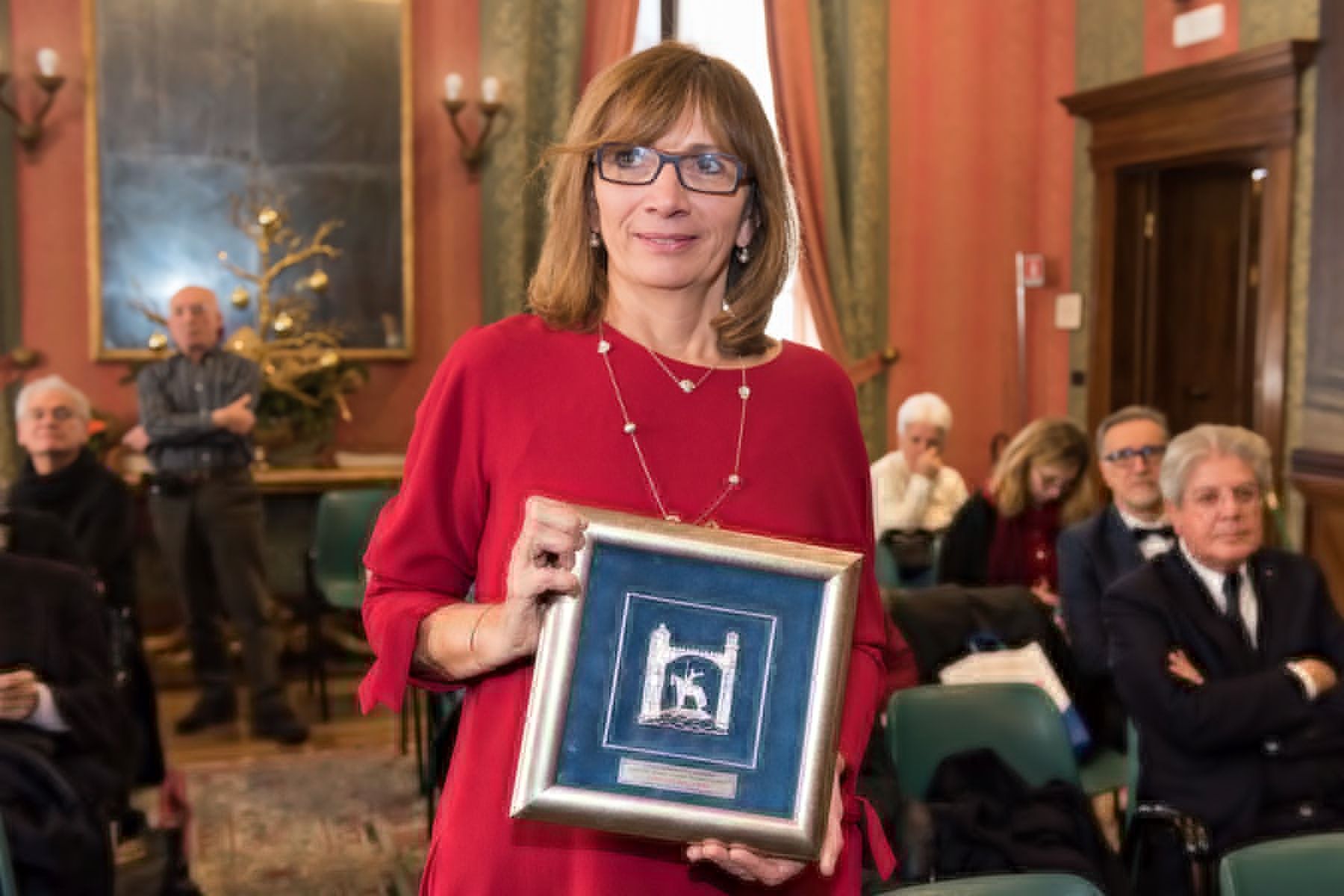 Una donna vestita di rosso tiene in mano una foto incorniciata di fronte a un gruppo di persone.