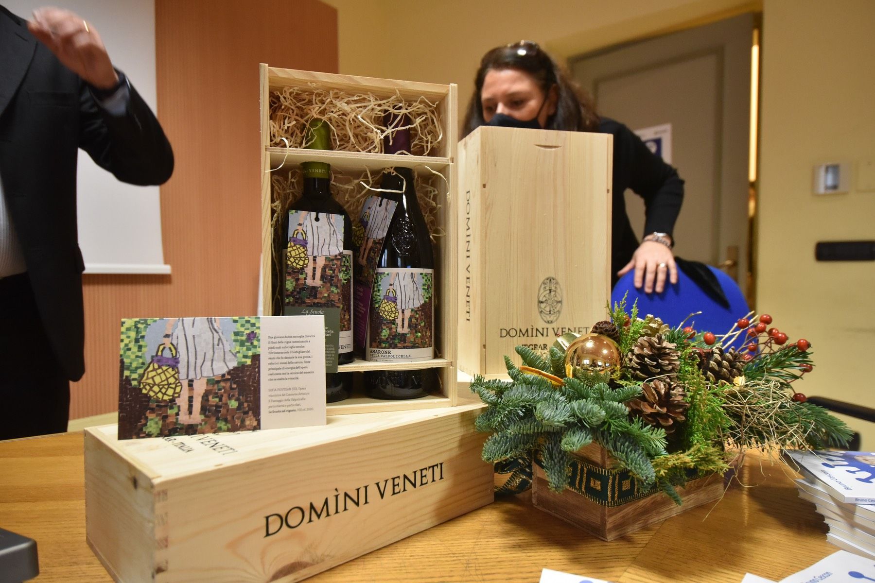 Una donna è in piedi accanto a una scatola di legno piena di bottiglie di vino.
