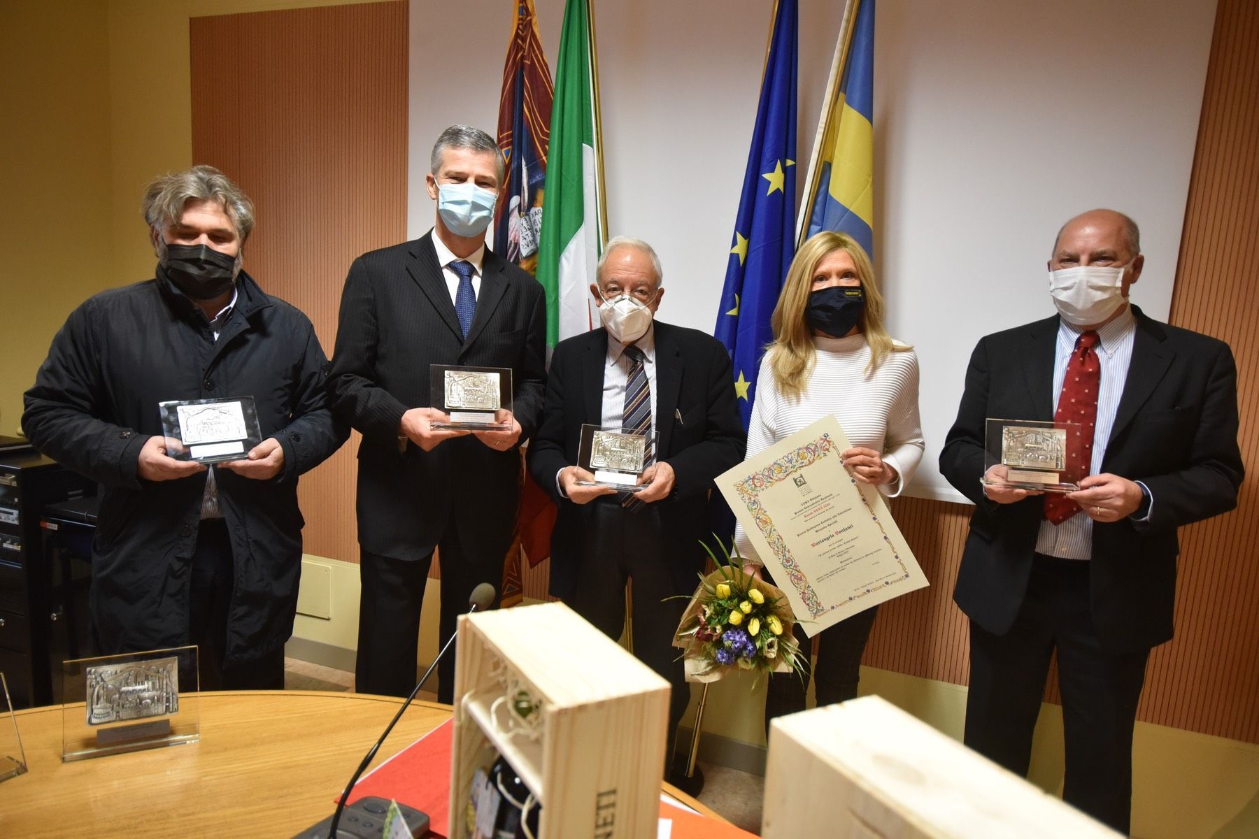 Un gruppo di persone che indossano maschere per il viso sono in piedi attorno a un tavolo con in mano dei premi.