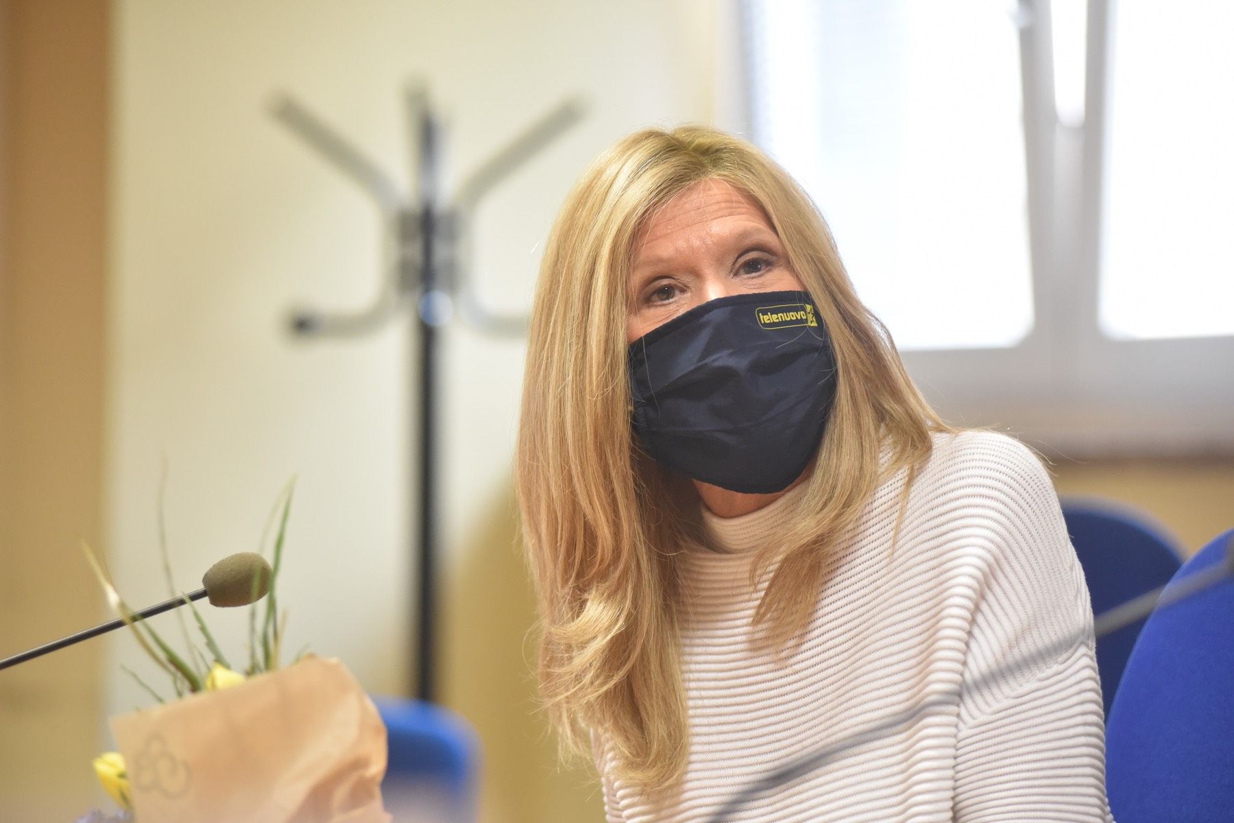 Una donna che indossa una maschera è seduta davanti a un microfono.