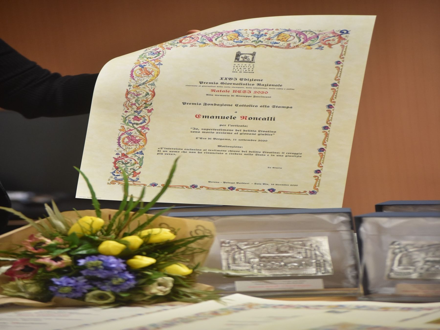 Una persona tiene in mano un certificato accanto a un mazzo di fiori