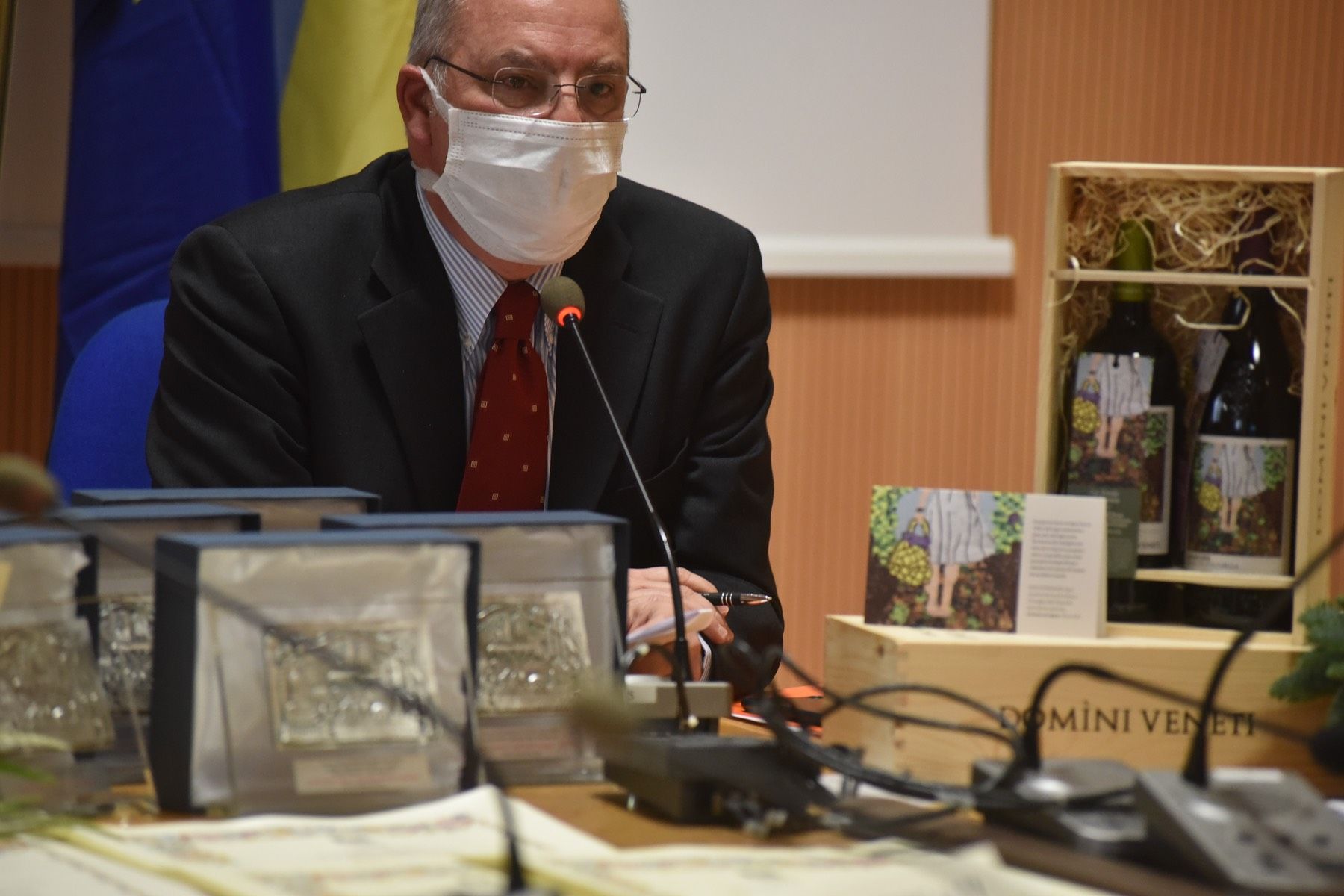 Un uomo che indossa una maschera è seduto a un tavolo con un microfono.