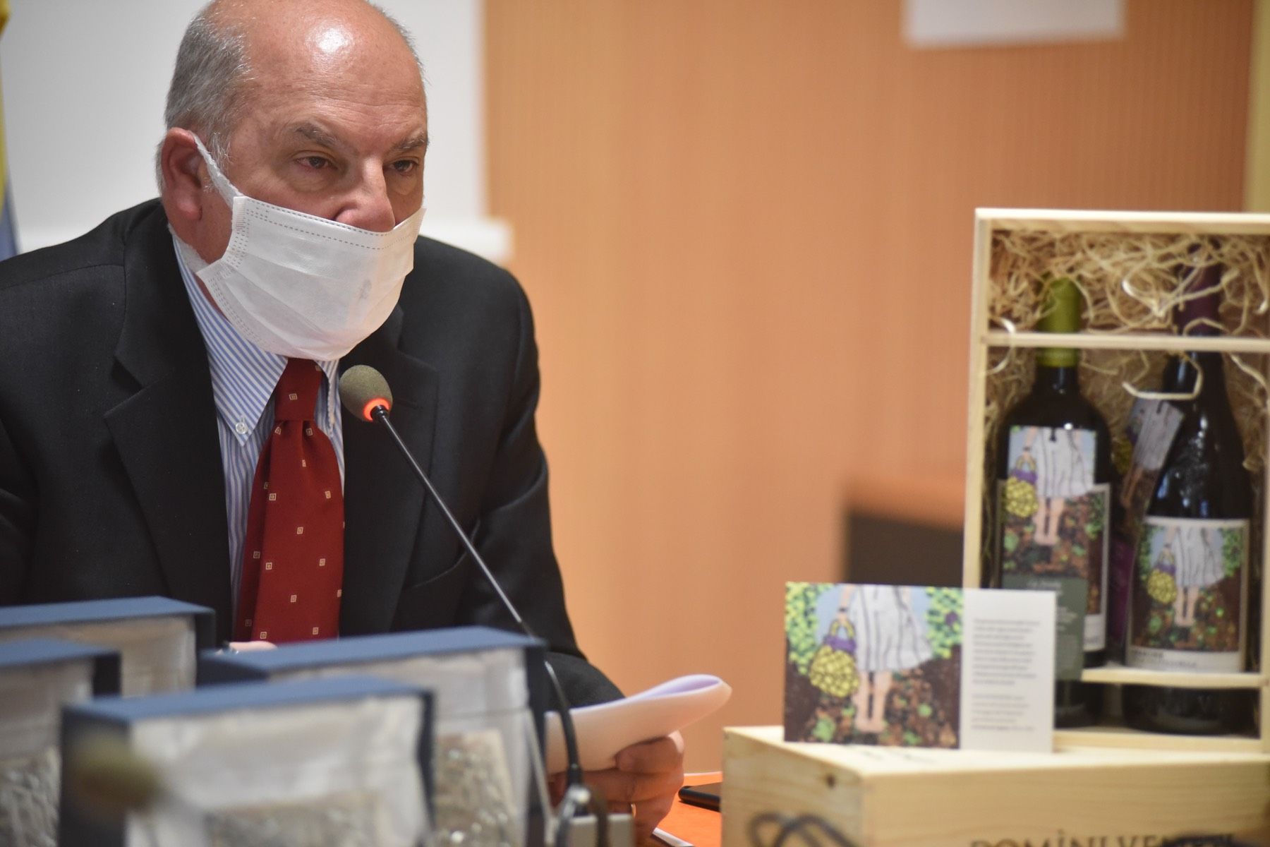 Un uomo che indossa una maschera è seduto a un tavolo con bottiglie di vino.