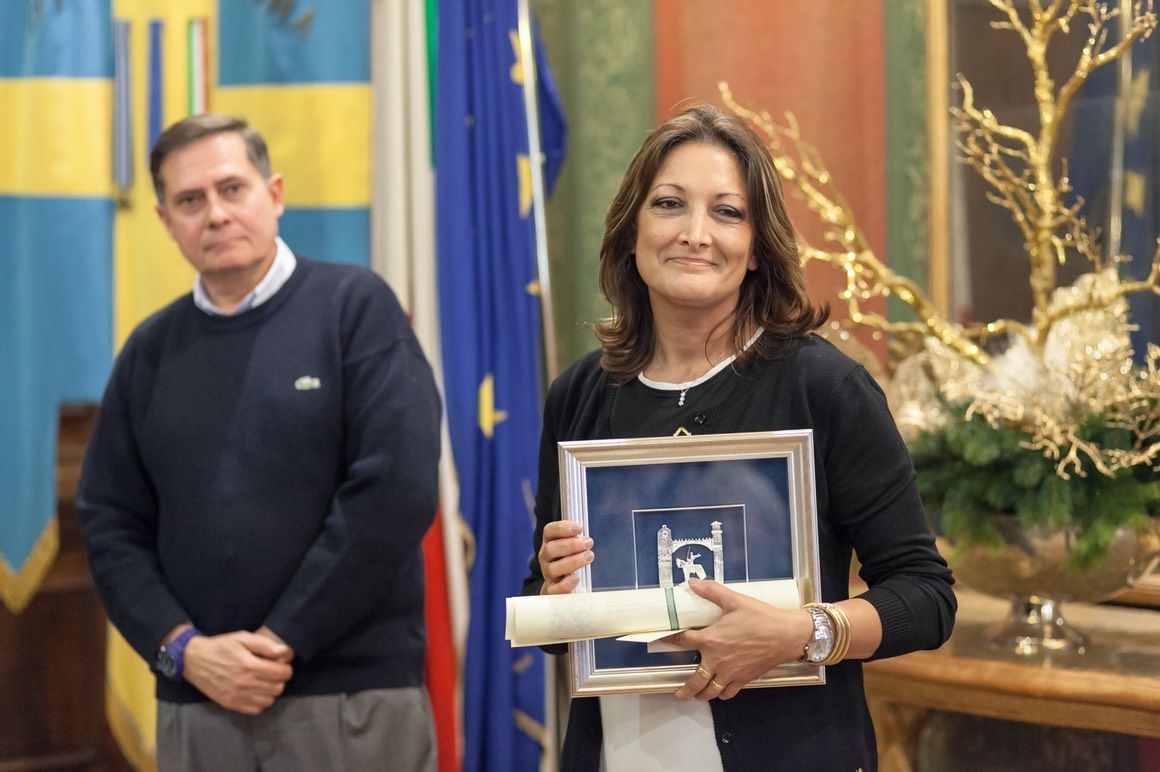 Una donna tiene in mano un certificato davanti a un uomo e bandiere.