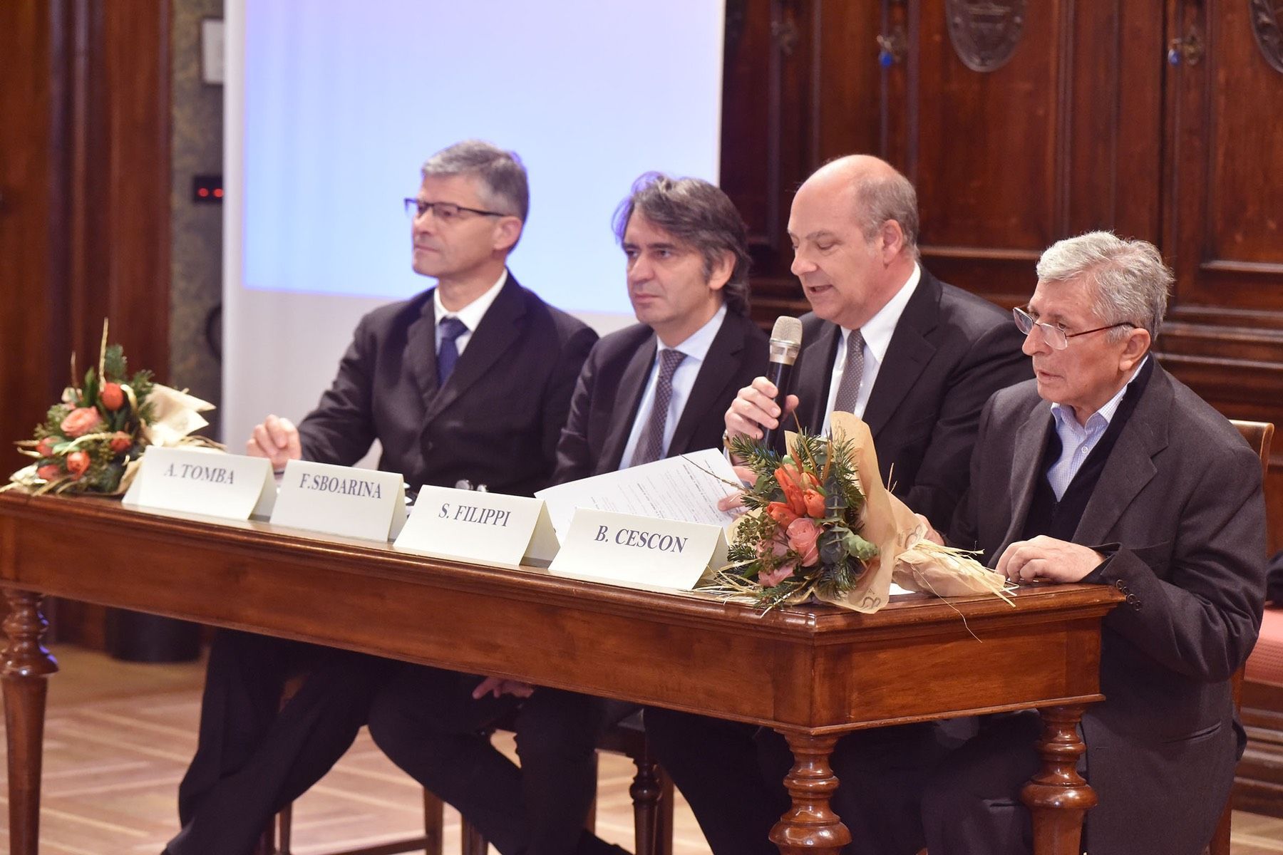 Un gruppo di uomini è seduto a un tavolo e parla ai microfoni.