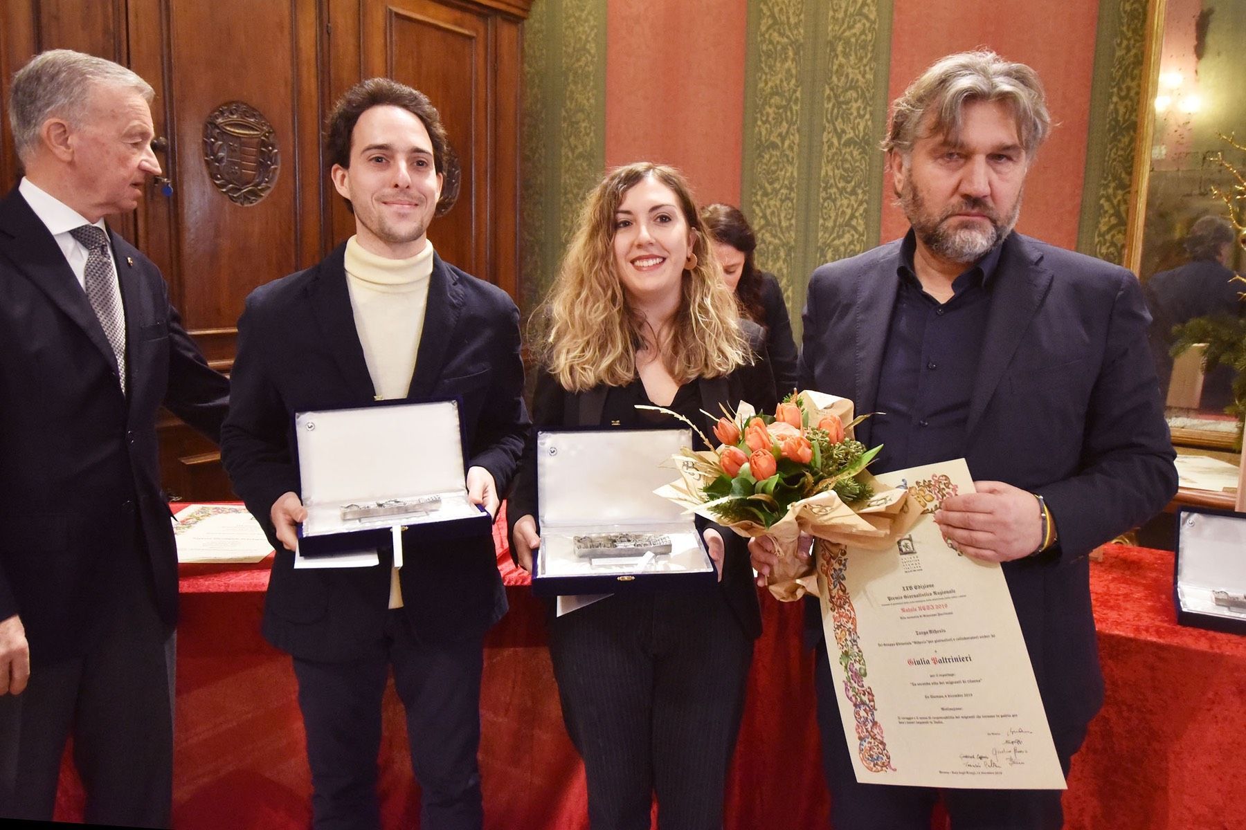 Un gruppo di persone in piedi una accanto all'altra con in mano fiori e targhe.