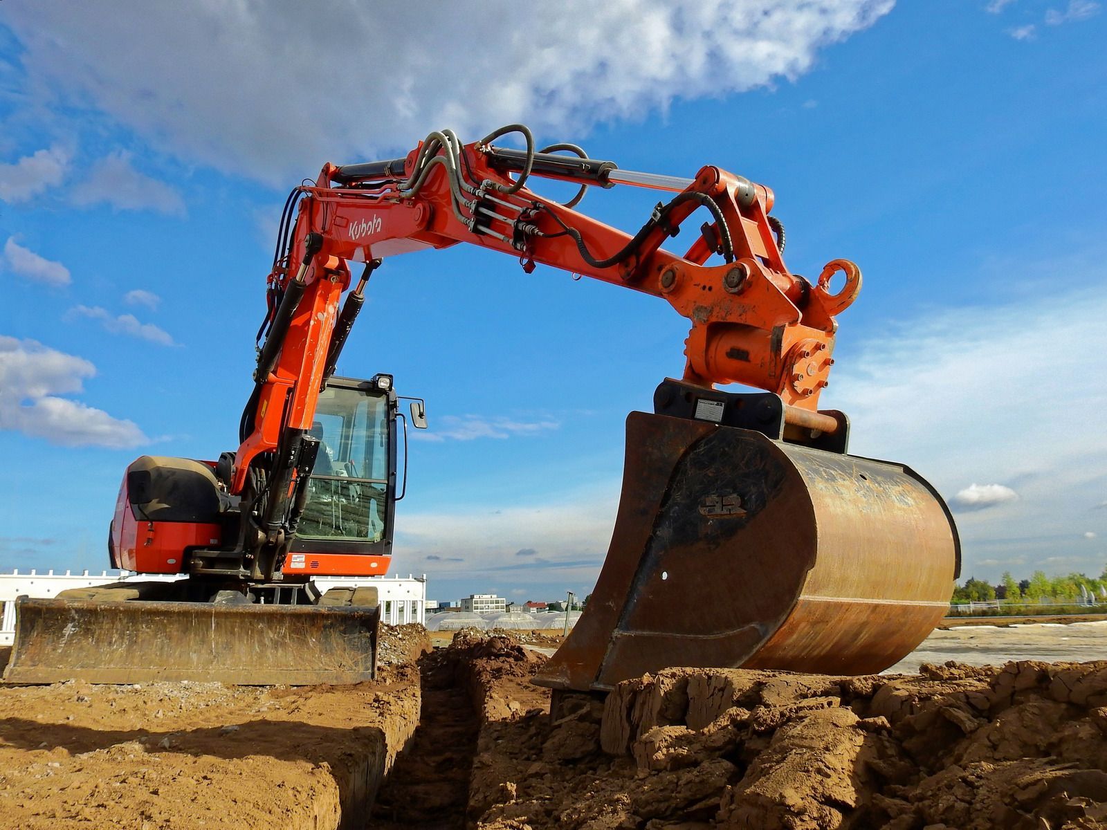 Orange excavator digging dirt at a construction site under a blue sky
