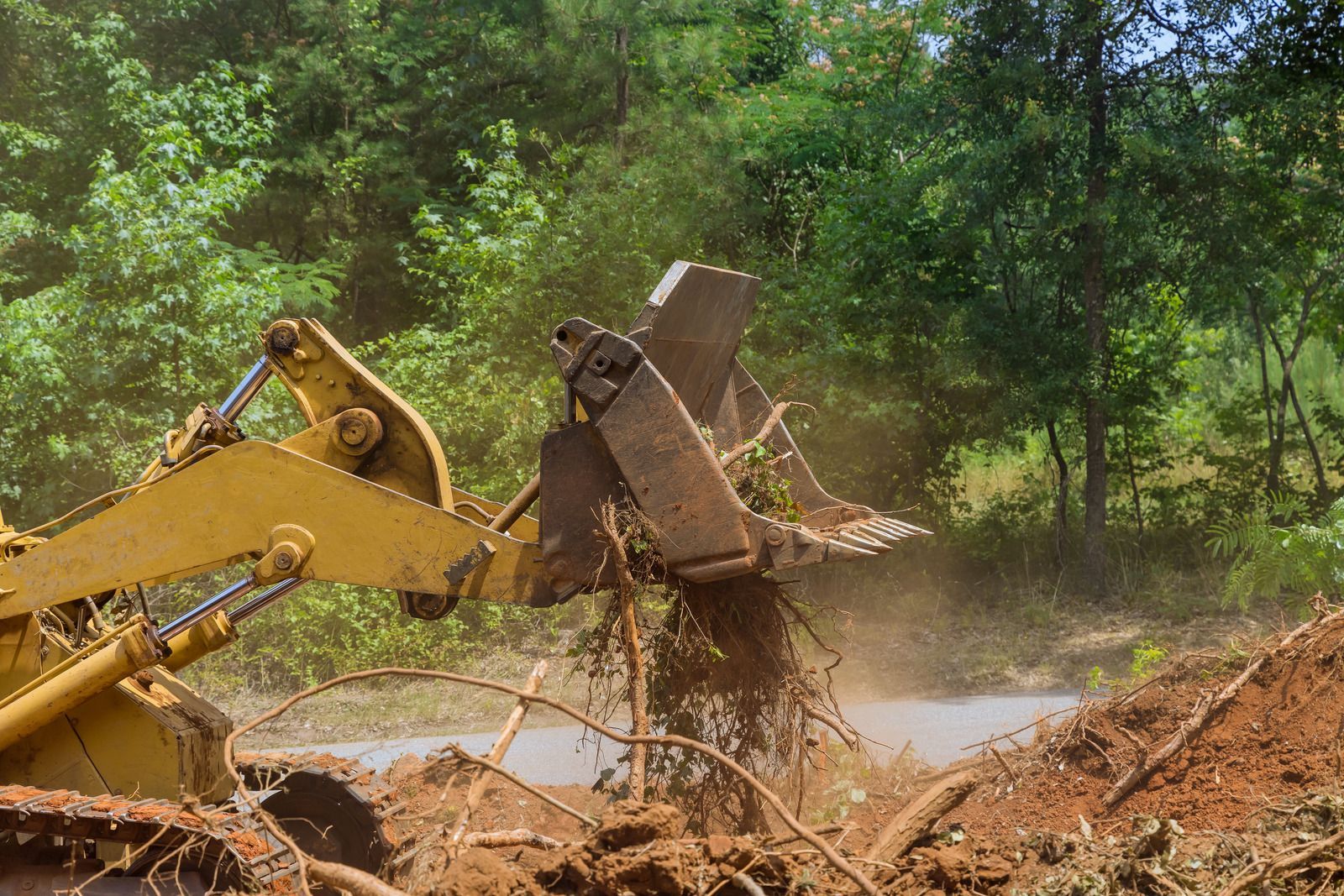 Yellow excavator digging muddy earth in a wooded area, with dirt and water spraying.