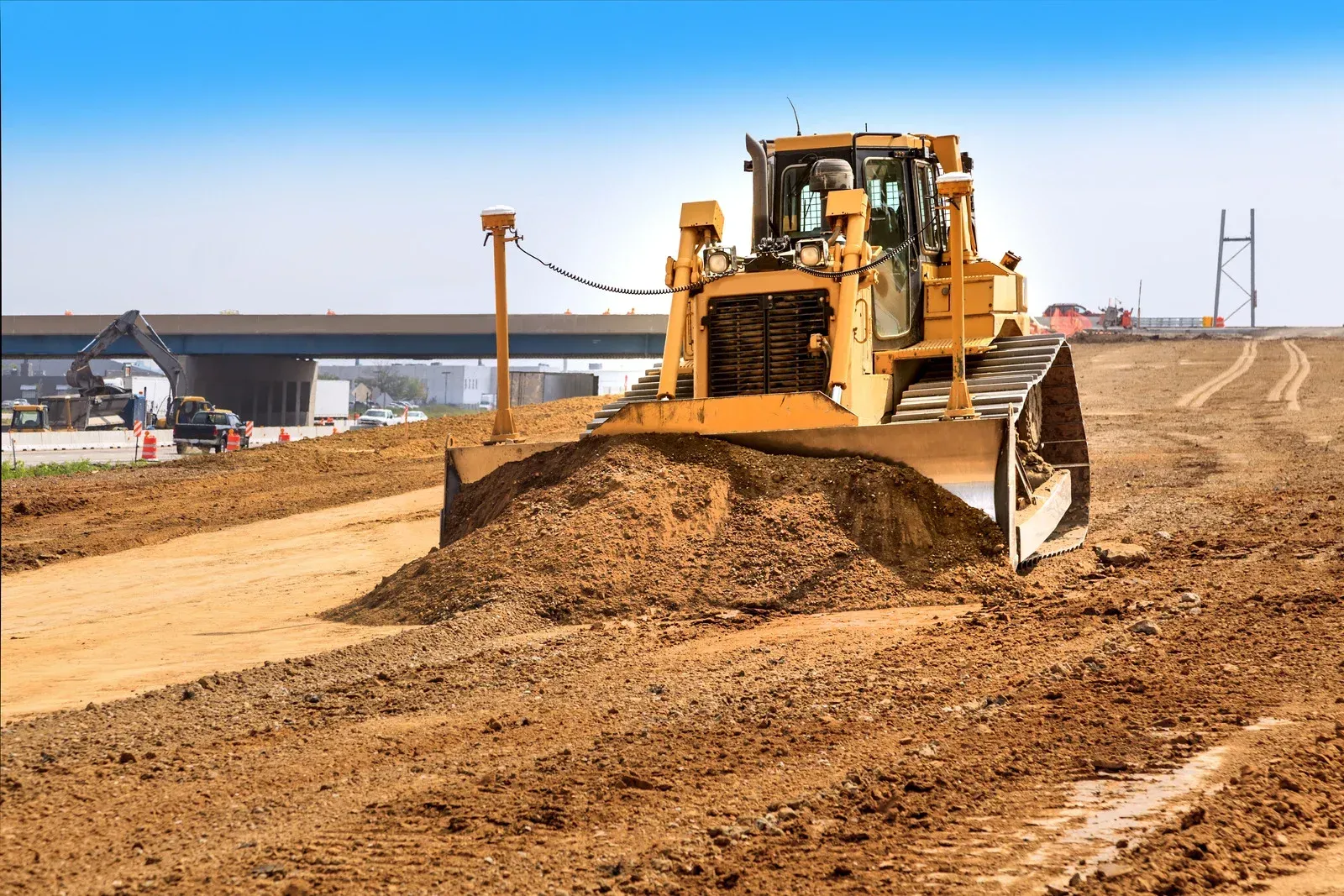 Yellow bulldozer grading a dirt road construction site under a clear blue sky