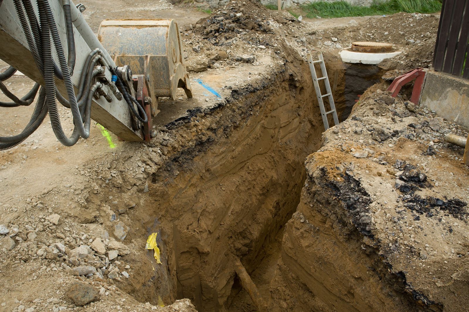 Deep trench dug in an outdoor construction site with exposed soil and equipment nearby