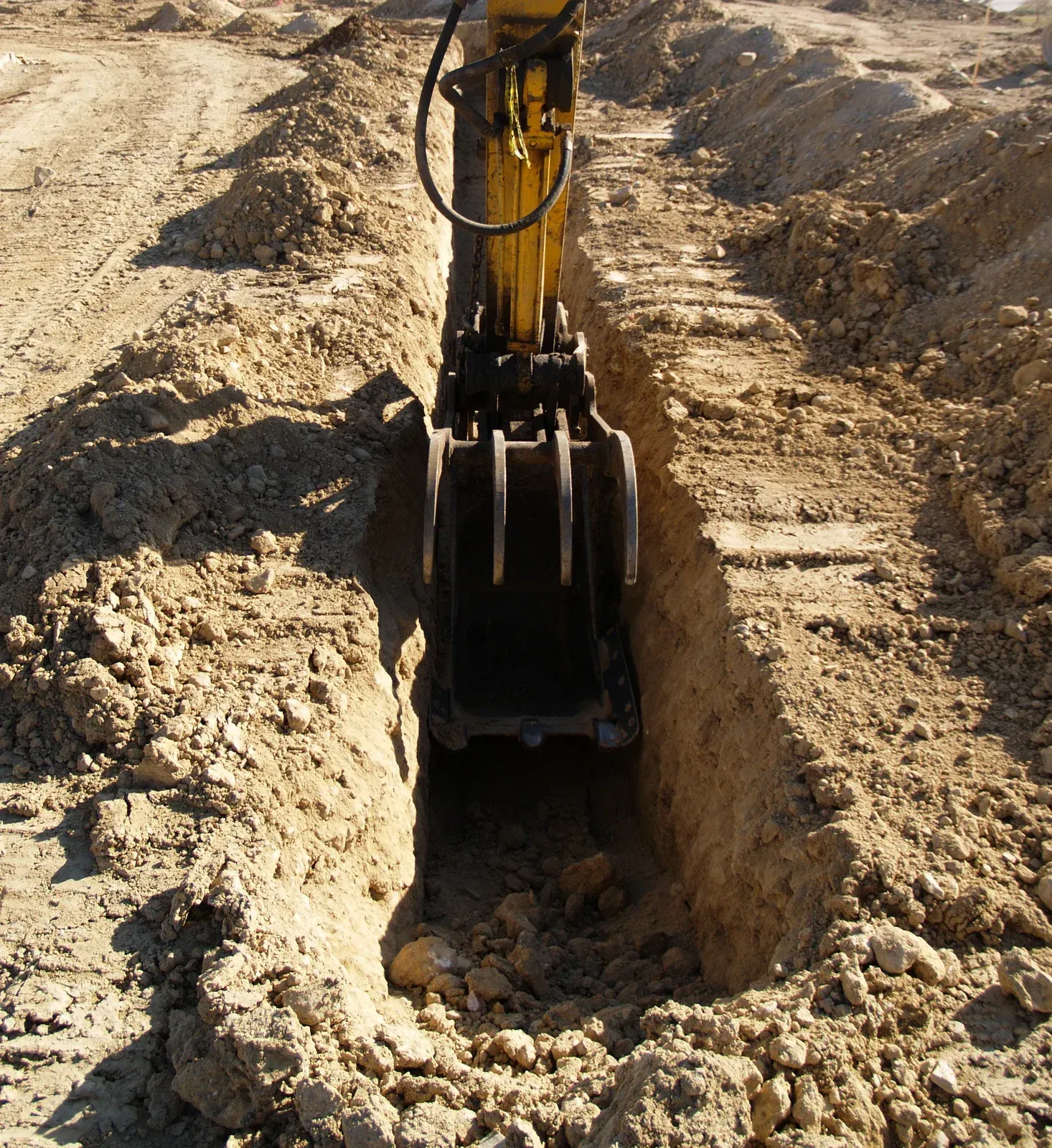 Excavator bucket digging a trench in dry dirt at a construction site