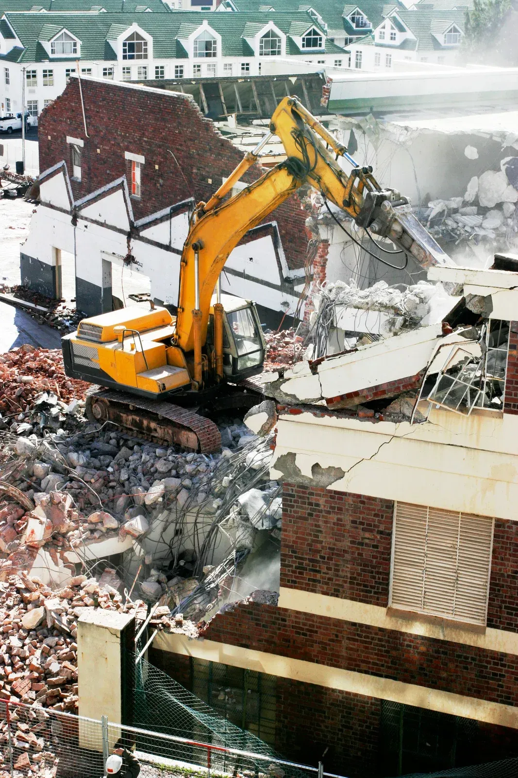 Yellow excavator demolishing a snowy brick building amid rubble and debris