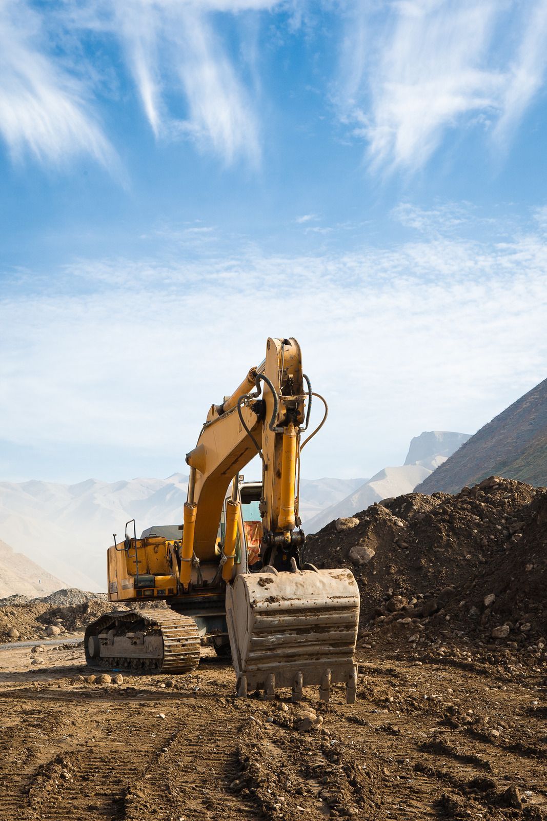 Yellow excavator at a dirt construction site under a blue sky