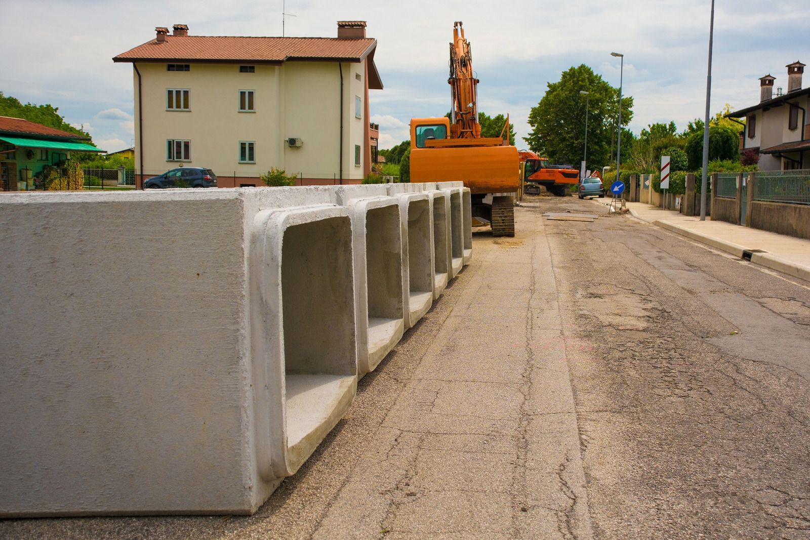 Concrete barriers lined along a dirt road at a construction site with an excavator in the background