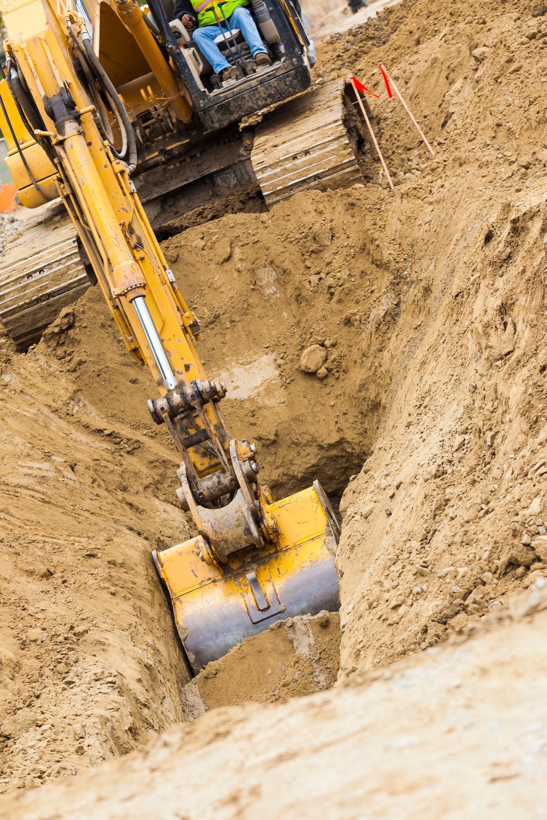 Yellow excavator digging a deep trench in sandy soil at a construction site