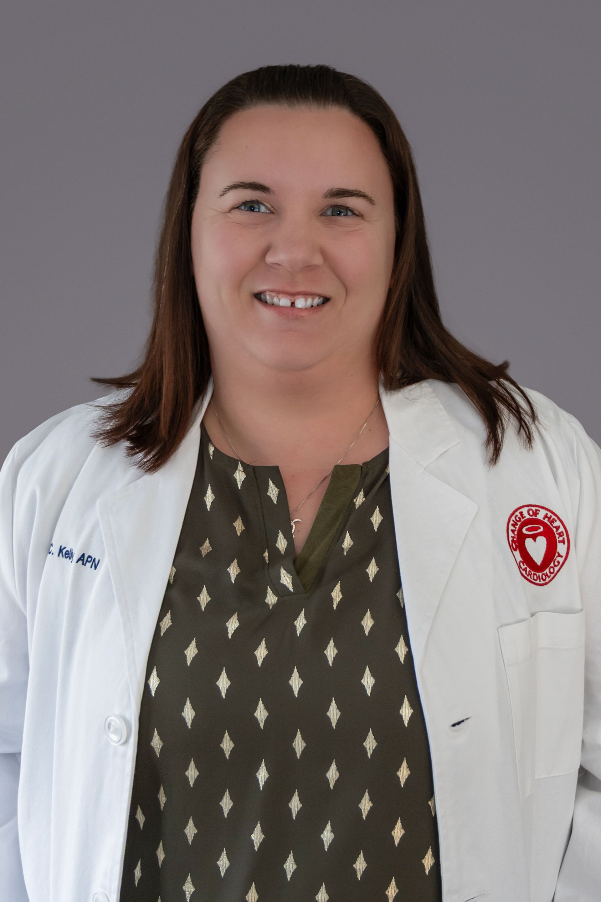 Woman wearing a white coat with a logo, smiling, and looking at the camera.