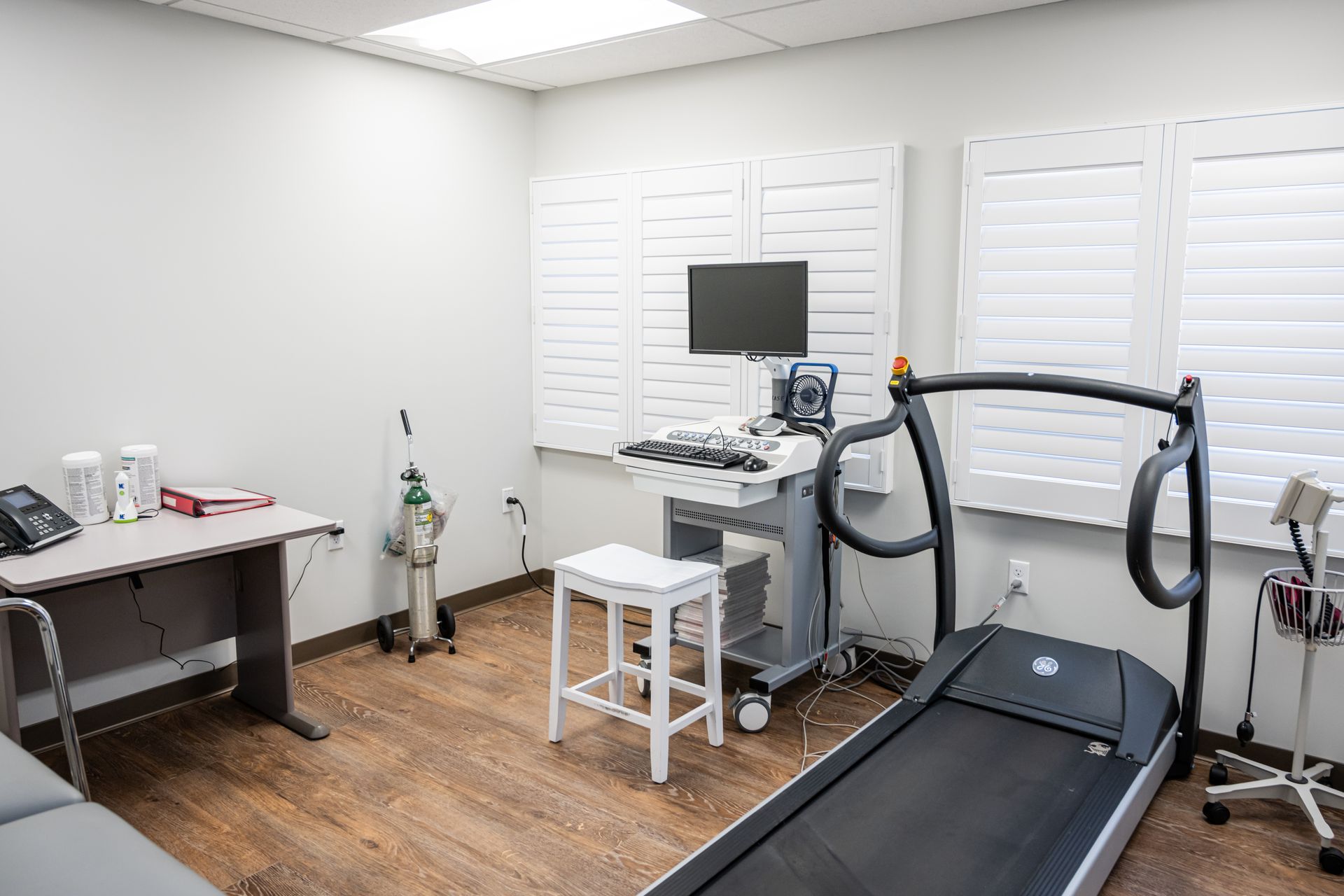 Medical exam room with treadmill, equipment, and a desk.