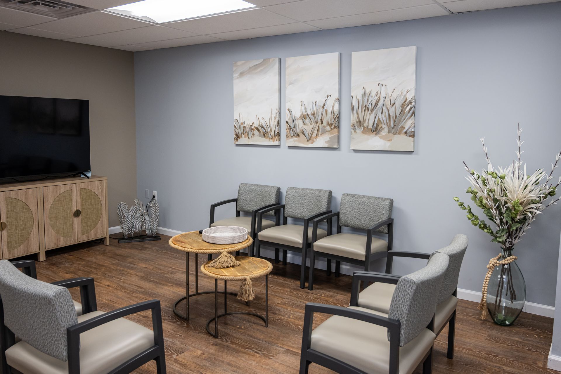 Waiting room with neutral color palette, chairs, art, TV, and decorative vase.