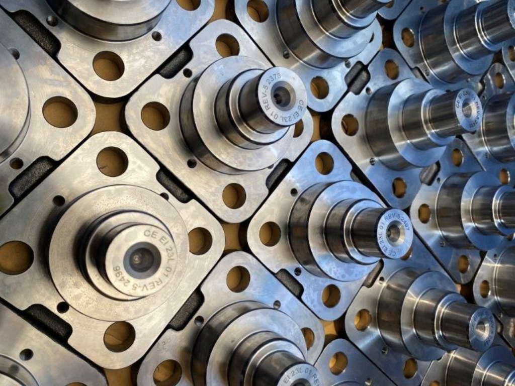 Primo piano di ingranaggi in metallo lucidato e componenti circolari di macchine disposti secondo uno schema industriale ripetitivo.