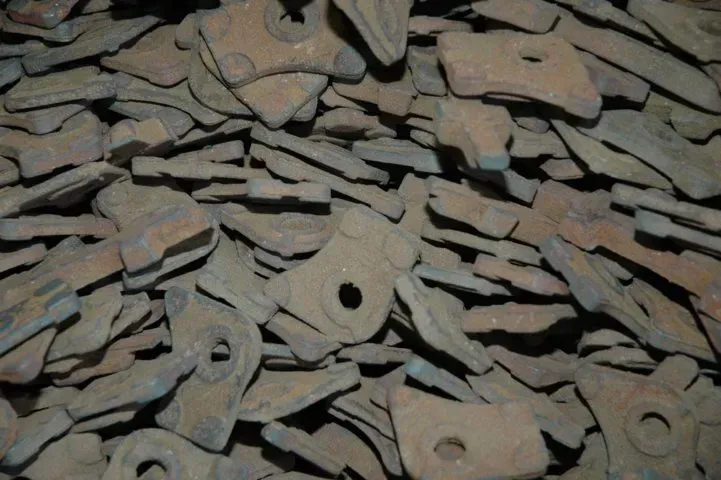 Un mucchio di ganci e pezzi piatti di metallo arrugginito accatastati sul terreno.