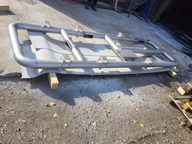 Struttura metallica grigia su blocchi di legno all'aperto su una superficie ghiaiosa, probabilmente un componente di un veicolo o di un'attrezzatura.