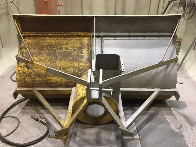 Grande tramoggia o spandiconcime in metallo arrugginito con telaio di supporto triangolare in un'officina