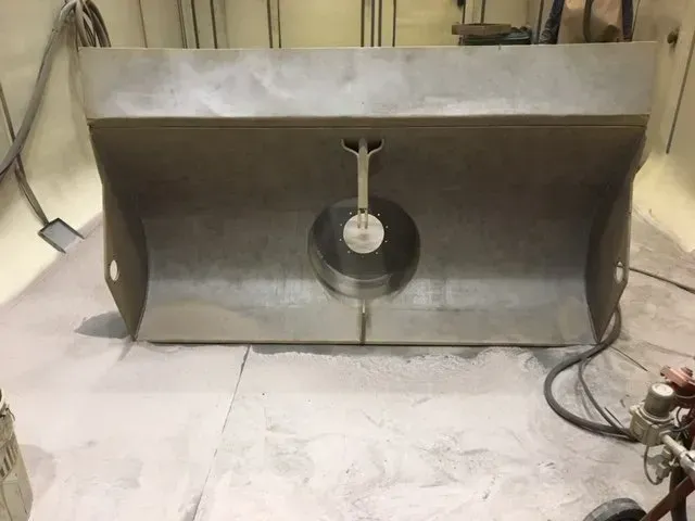 Un lavello in acciaio inox con scarico centrale in un locale di servizio, con tubi flessibili e idraulici sulla destra.