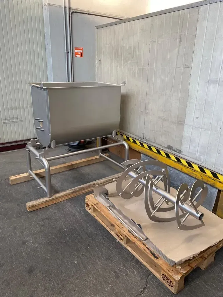 Attrezzature industriali su un pallet accanto a un contenitore metallico in un angolo di un magazzino con una striscia di segnalazione a muro.