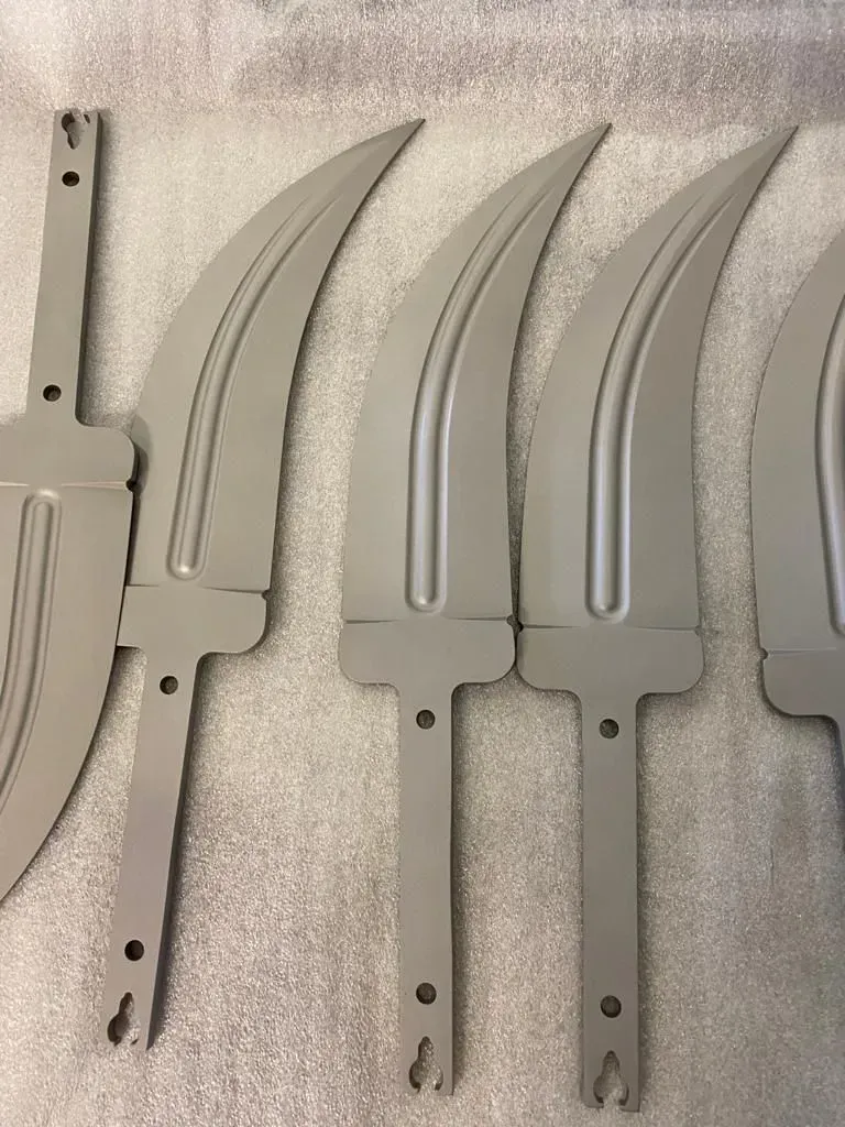 Quattro elementi metallici grigi, curvi e simili a lame, disposti su una superficie bianca ruvida.