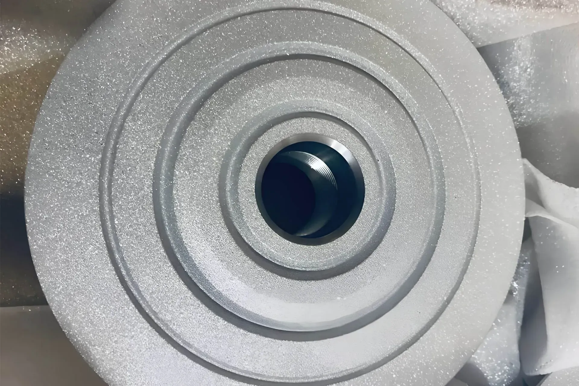 Primo piano di una puleggia in metallo argentato con un foro centrale, avvolta in un imballaggio di schiuma.
