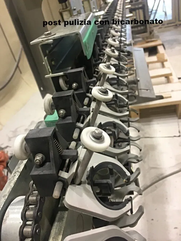 Linea di macchinari industriali con componenti e ruote in metallo nero e argento in un corridoio di officina.