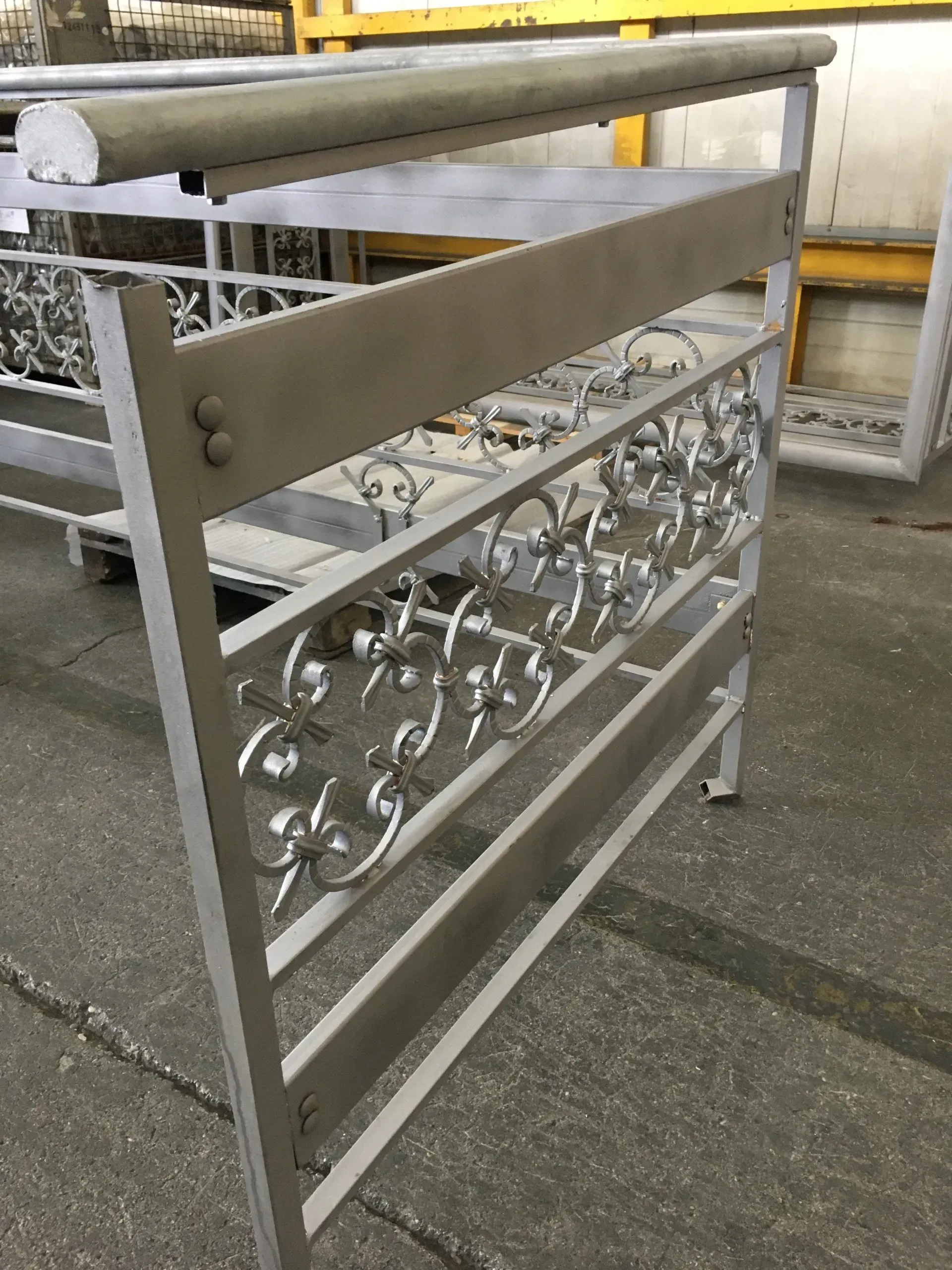 Cancello in metallo bianco con decorazioni a volute e pannello beige in un'area industriale esterna.