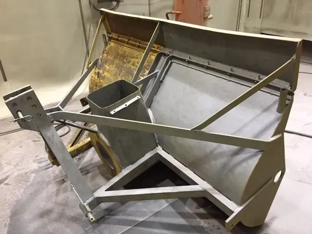 Struttura metallica industriale a tramoggia o scivolo, composta da pannelli angolati e telaio, situata in un'officina.