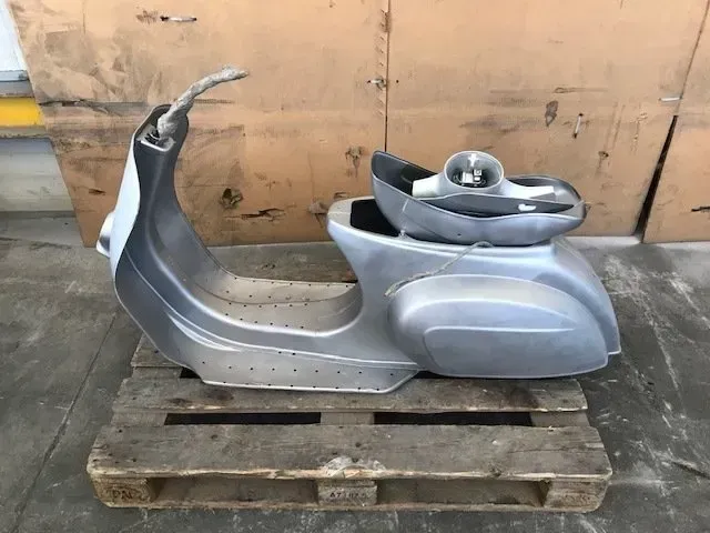 Carrozzeria di scooter color argento su un pallet di legno in un contesto industriale.