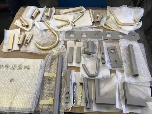 Vari componenti di ferramenta per porte, di colore bianco e argento, disposti su un tavolo, avvolti in pluriball e schiuma.
