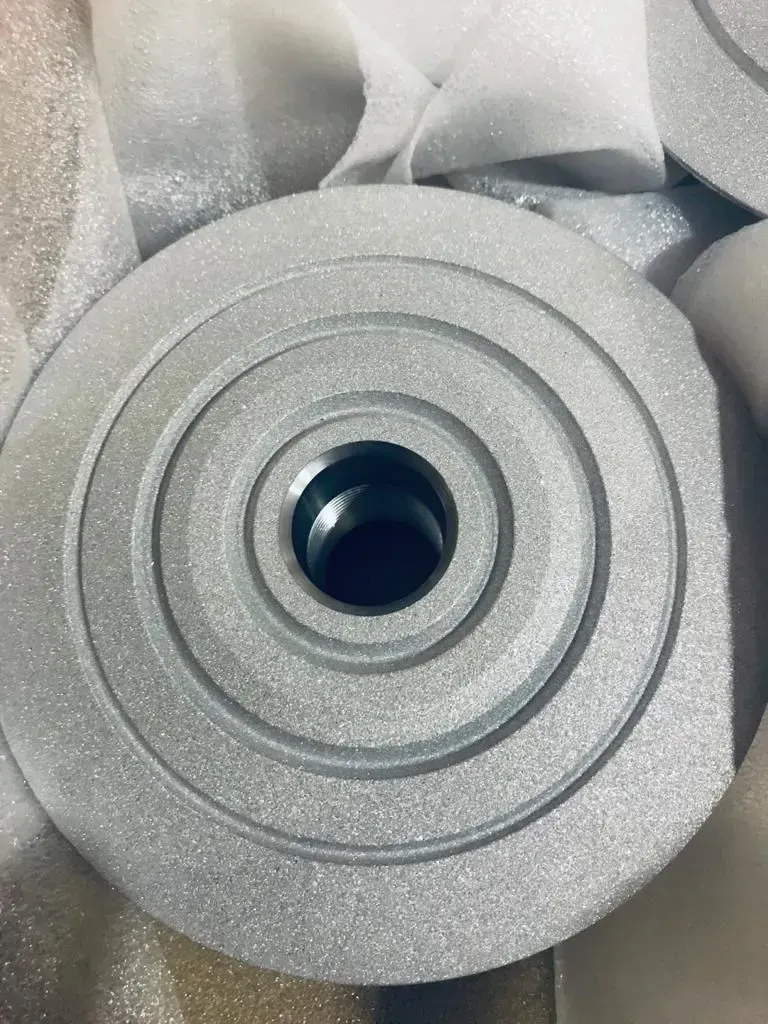 Primo piano di una ruota o puleggia in metallo argentato con un foro centrale, avvolta in un imballaggio di schiuma.