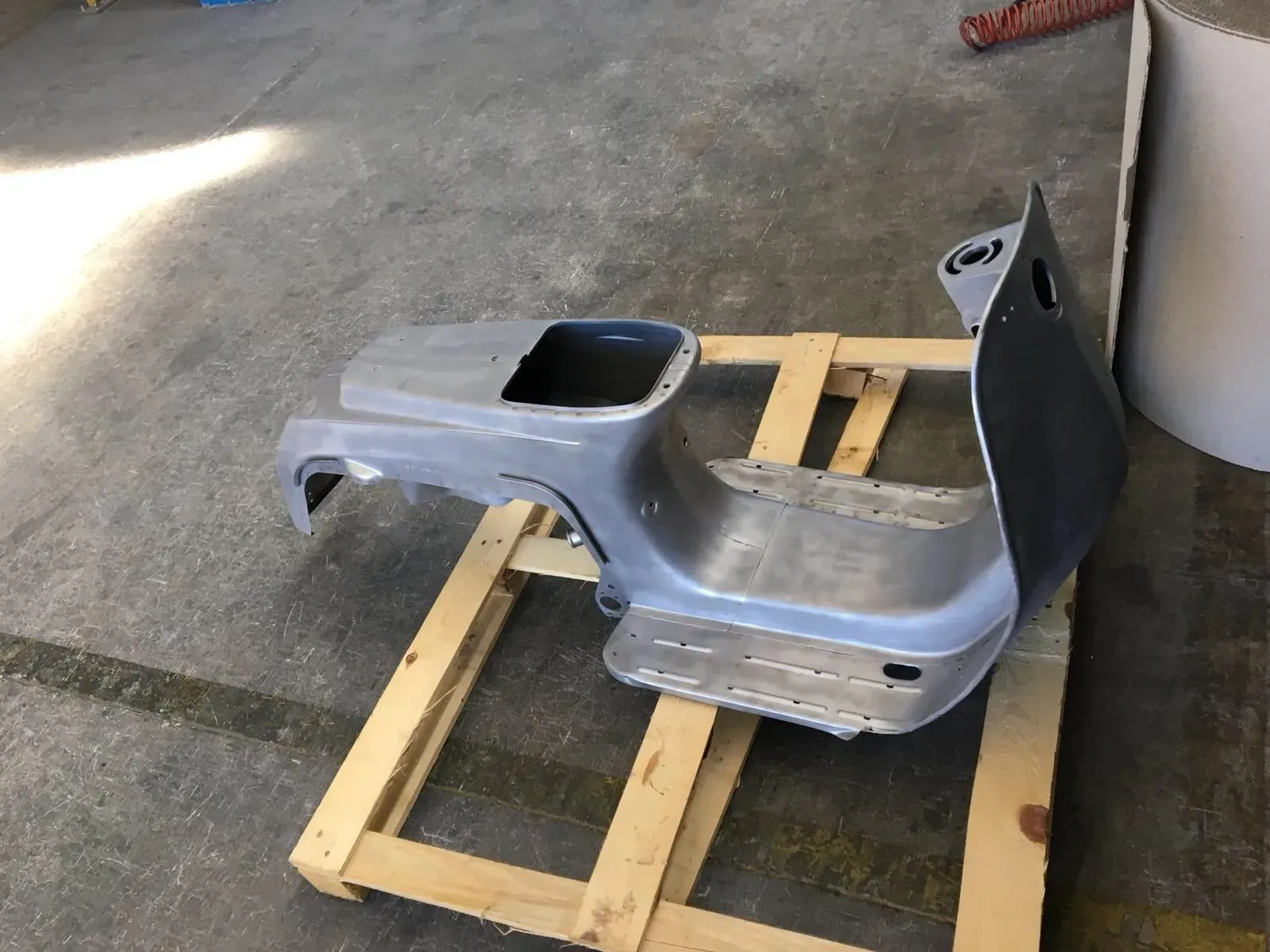 Un pannello di carrozzeria grigio stampato poggia su un pallet di legno in un ambiente simile a un garage.