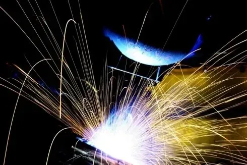 Brillanti scintille di saldatura esplodono su uno sfondo scuro con striature blu e gialle