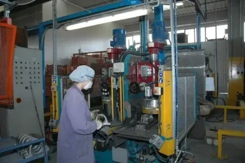 Operaio con elmetto bianco che aziona un grande macchinario industriale in una fabbrica con tubi e pannelli di controllo.