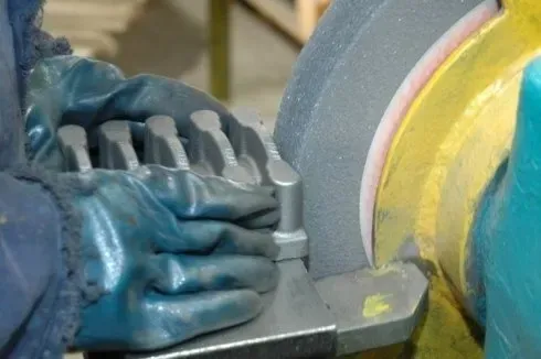 Mani guantate al lavoro su una mola in un'officina, tra macchinari blu e gialli.