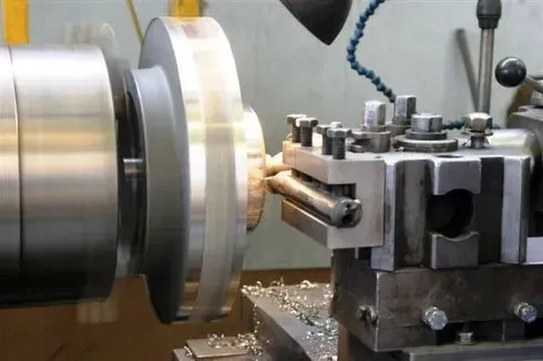 In un'officina, un tornio per metalli lavora un pezzo cilindrico con utensile da taglio e trucioli di metallo.