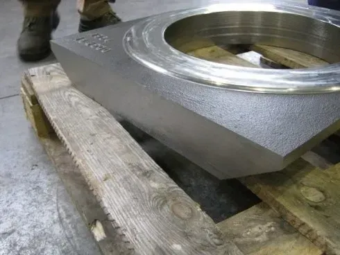 Grande blocco di metallo con un'apertura circolare ricavata tramite lavorazione meccanica, appoggiato su un pallet in un'officina.