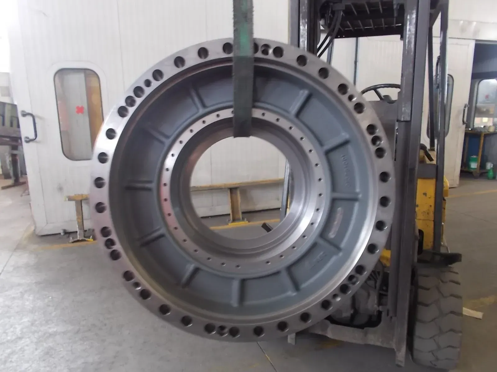 Grande rotore di macchina industriale grigio con fori per bulloni in un magazzino, parzialmente montato su un'attrezzatura